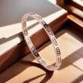 Dettaglio macro del motivo a greca in oro rosa sul bracciale rigido in acciaio titanio - Oro rosa
