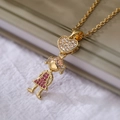 Collar bañado en oro con colgante de corazón y niña en circonitas sobre elegante tela blanca - Estilo Corazón de Niña Dorado