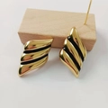 Detailed close-up of 18K gold plated wing earrings with black enamel on a wooden display - Gold with Black