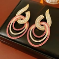Close-up of golden geometric earrings with white and pink crystals on black leather box - Silver Earring Post Style / Gold-Red