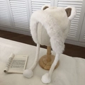Detail of white plush bear ear hat featuring long tassel balls on a wooden stand - Double Sphere Style / White