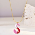 Macro shot of gold S-letter pendant with pink and red enamel on a stone surface - S