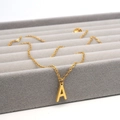 Makroaufnahme einer goldenen Halskette mit Buchstabe A auf einem grauen Samttablett - Buchstabe A / Gold
