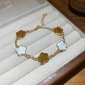 Détail d'un bracelet fleuri doré avec des breloques en émail blanc et ambre poli - Cinq Fleurs / Blanc-Café