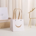 Weiße quadratische Papiertüte mit Smiley-Ausschnitt und braunen Kordelgriffen - Smiley Weiß 10x10x10cm