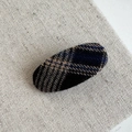Vue détaillée d'une barrette ovale à motif écossais en laine beige sur fond en lin - Clip Bec de Canard Ovale à Carreaux / Noir