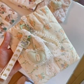 Detailed close-up of quilted floral cosmetic bag with lace trim and heart pendant - Orange Pink Floral