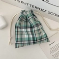 Close-up of a plaid drawstring storage pouch for jewelry and earphones on a desk - Green Black Plaid (Small)