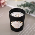 Scented soy candle in a matte black glass jar with white floral label and dust cover - Blackberry & Bay