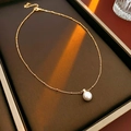 Detalle de collar de cadena de bolas doradas con perla blanca sobre soporte de cuero - Dorado