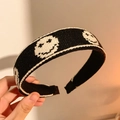 Serre-tête tricoté noir et blanc avec motifs souriants tenu à la main par une personne - Visage souriant