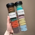 Hand holding two transparent jars of colorful high-elastic hair bands in varied shades - Forest + Spring Series (200 Pcs/Can)