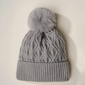 Vista detallada del gorro de punto gris con pompón de pelo sintético y diseño trenzado - Talla única / Gris