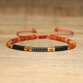 Adjustable woven bracelet with orange cylinder stones and black beads on wooden surface - No.65 Red Agate & Matte Black
