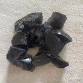 Detailed close-up of natural black obsidian raw stones with glass luster on soft fabric - Black Agate
