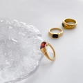 Detail of gold rings with red and black gemstones on a textured glass pedestal - US 6 / Red Zirconia