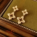 Macro shot of gold-plated rhombus flower earrings with brushed texture and zircon stones - Gold