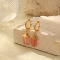 Detalle de pendientes de aro dorados con colgantes de piedra rosa sobre piedra beige - Redondo Plano Rosa