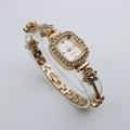 Detail of square gold bracelet watch featuring a crystal bezel and floral links on a stand - Rose Gold Case White Dial