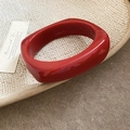 Detail of a thick square-edged bright red resin bangle on a textured ceramic tray - Red