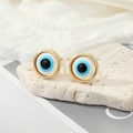 Primer plano de pendientes Evil Eye dorados con incrustación de resina azul en piedra - Ojo Blanco Dorado