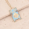 Macro view of gold tarot card necklace with blue enamel and colorful gemstone accents - The World-Blue
