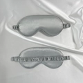 Glossy silver grey satin sleep eye mask with elasticated strap shown on silk background - Gray