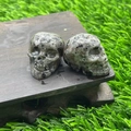 Polished natural speckled stone crystal skulls on a dark wood base with green lawn - Flame Stone
