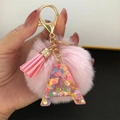 Close-up of pink pompom keychain with transparent letter A pendant and colorful heart sequins - Letter A