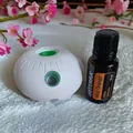 Close-up of portable white aroma diffuser with a 15ml essential oil bottle on fabric - Elegant White Sensor Machine + Wild Orange Essential Oil Set / 132.0
