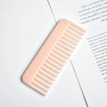 Close-up of pink marble pattern cellulose acetate wide-tooth comb on an open book - Peach Pink Pattern