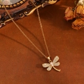 Detail der goldenen Libellenkette mit glitzernden Kristallen und weißen Perlen auf Samt - Gold Weiße Zirkonia Libellenkette (T031)