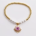 Bracciale di perle dorate con perle bianche e ciondolo occhio rosa su sfondo bianco - Rosa