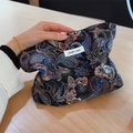 Dettaglio di una pochette in broccato tenuta in mano con ricami di farfalle colorate - Nero con motivo floreale a farfalla blu beige rosso