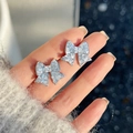 Vue détaillée des boucles d'oreilles papillon en argent avec cristaux sur la main - Clou de Boucle d'Oreille Nœud Strass (16#) / Argent/Bleu