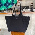 Detail of a black canvas tote bag with merciparis label on a cafe wooden stool - Large Black Plaid