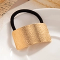 Black elastic ponytail holder with textured gold metal plate on white ceramic plate - Gold - Hammered Arc