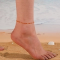 Close-up of orange beaded turquoise anklet on ankle at beach with sea waves background - Orange
