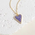 Close-up of golden heart pendant with purple shell mosaic and zircon border on stone base - Purple
