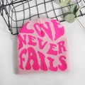 Pink knit beanie with bold magenta LOVE NEVER FAILS jacquard pattern on a white table - One Size / Light Pink