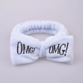 Macro detail of soft light blue plush headband featuring black OMG! embroidered bow - Blue