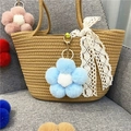 Close-up of colorful plush flower charms with gold metal clasps on a woven bag - Sky Blue