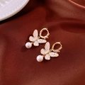Detail van gouden vlinder oorbellen met wit emaille en hangende parel hangers - Gouden Vlinder Huggies