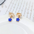 Elegante blaue Blumen-Ohrclips mit weißen Perlen und Goldfassung auf keramischem Teller - Clip-Ohrringe