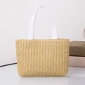 Detail of handwoven straw tote bag with white ribbon handles on a glass surface - Horizontal / Khaki