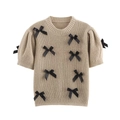 Gros plan sur la texture en maille et les nœuds en satin noir du pull-over de couleur beige - Kaki