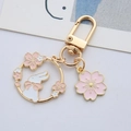 Nahaufnahme vom goldenen Kirschblüten-Schlüsselanhänger mit weißem Hasen und rosa Blumenanhänger - Fliege Hase Ringschloss