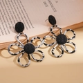 Detail view of flower-shaped zebra print fabric earrings with gold metal on a book - Coffee