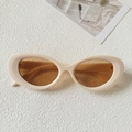 Flat lay of vintage oval sunglasses with cream frames and amber lenses on a white textured surface - Off-white