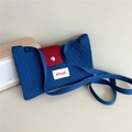 Close-up of blue knitted crossbody bag with red flap, metal button and Hilldi label - Dark Blue